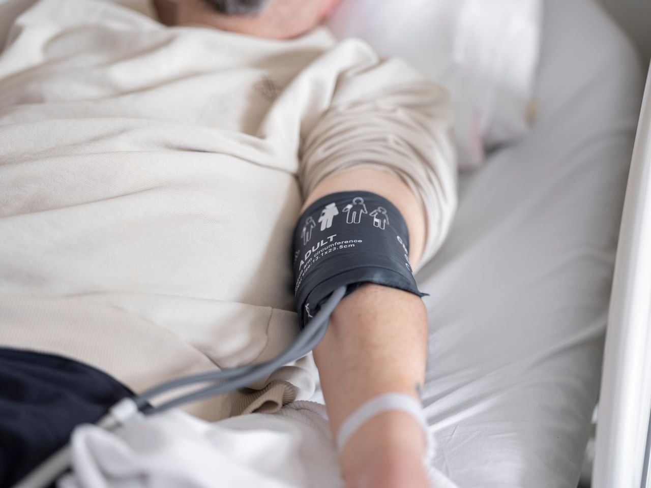 services-04 Close-up of patient in hospital bed with blood pressure cuff on arm, emphasizing healthcare theme.