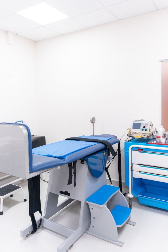services-03 Clean and well-equipped hospital examination room with blue medical equipment and diagnostic devices.